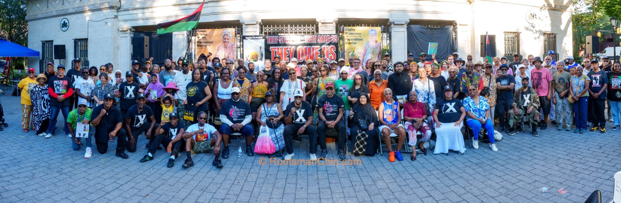 Group photo of rally attendees in front of the "They Owe Us" banner